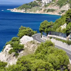 Krzewiasty, skalisty brzeg z krętą drogą i błękitnym morzem.