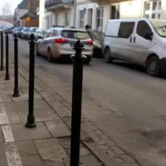 Słupek chodnikowy, radiowóz i biały van na ulicy.