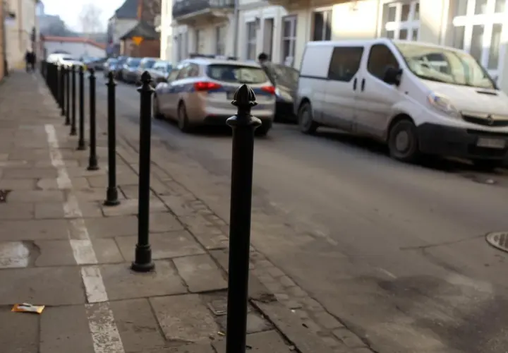 Słupek chodnikowy, radiowóz i biały van na ulicy.