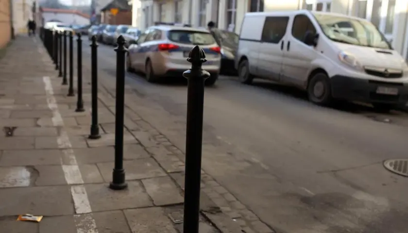 Słupek chodnikowy, radiowóz i biały van na ulicy.